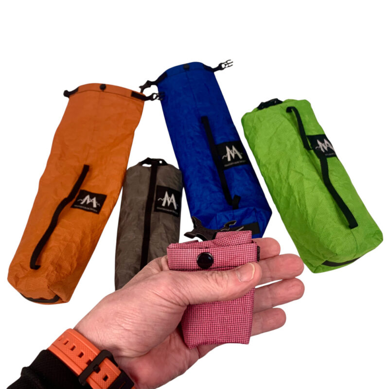 Various colors and sizes of Ultra Fork Dry Bags with one folded tiny in a hand in the foreground